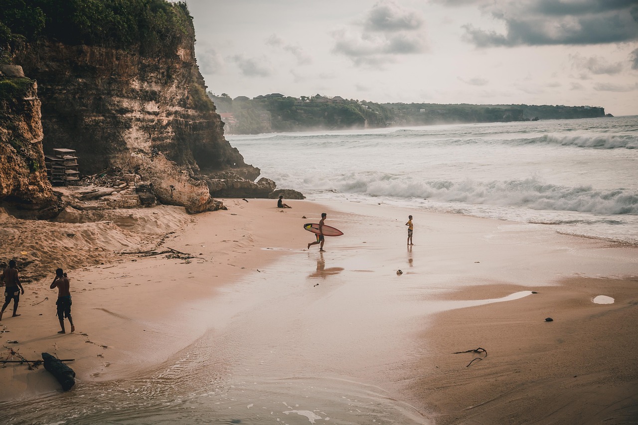 Uluwatu Bali clifftop beach with surfer carrying a board across golden sand