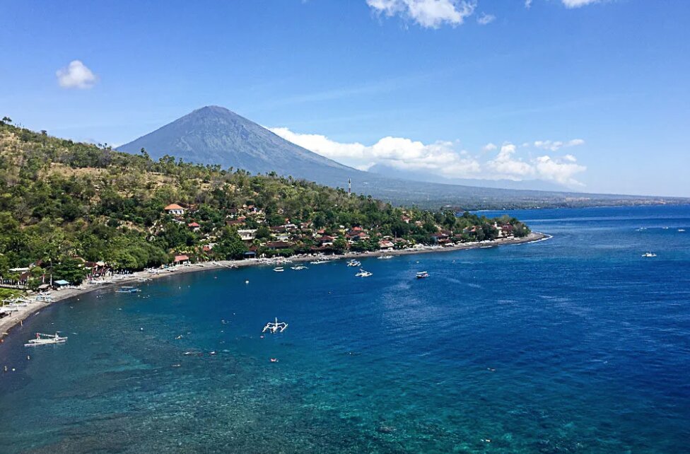 Amed Coast — Mount Agung rising above black-sand beaches and fishing boats on Bali's north-east shore